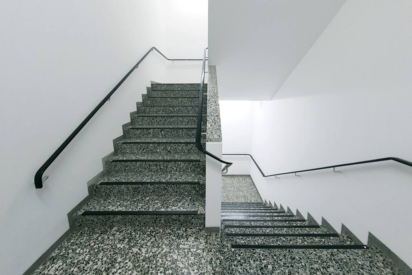 Helles Treppenhaus mit Terrazzostufen und schwarzem Handlauf